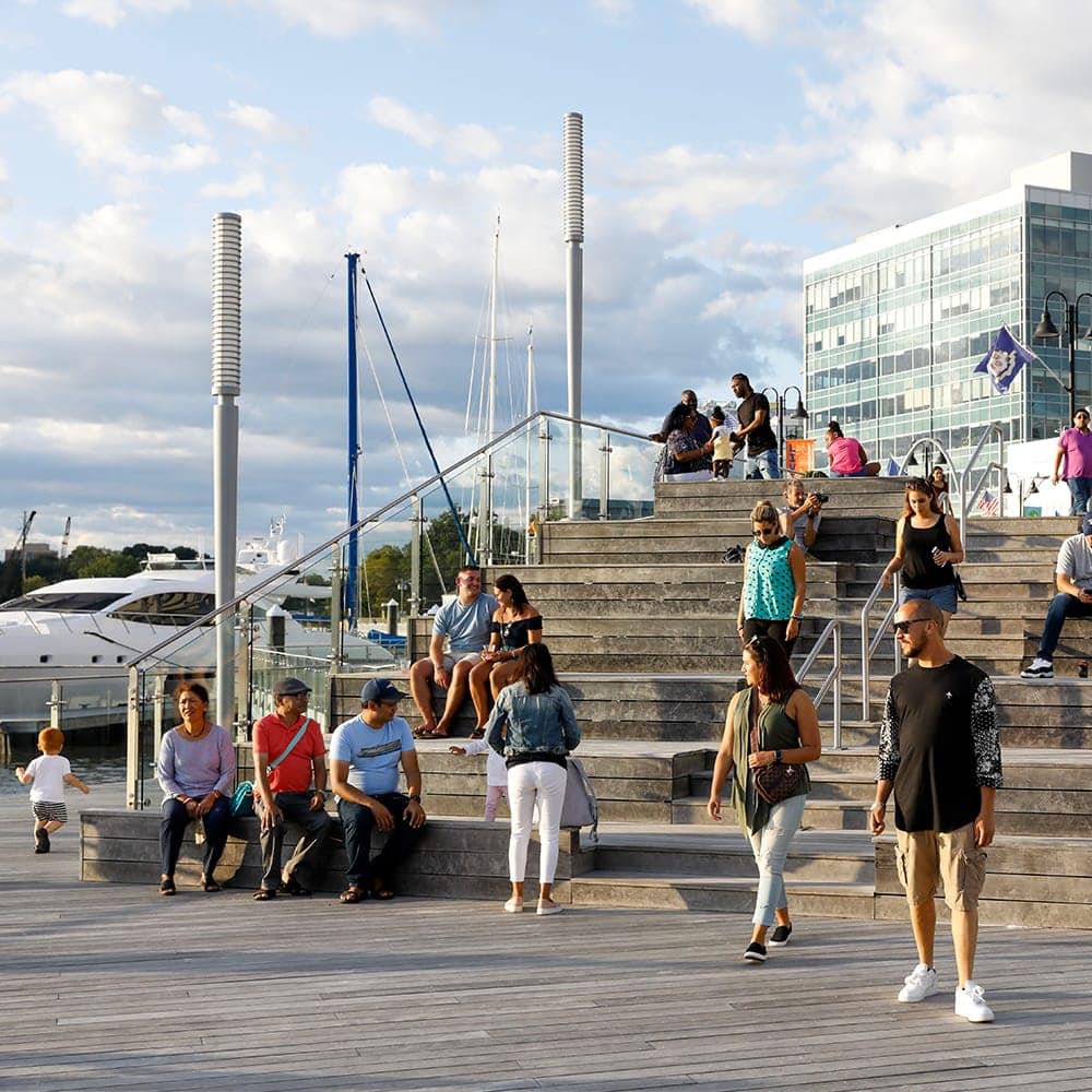 A crowd of people utilize concrete stairs by the water