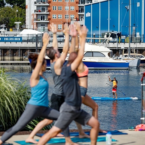 A large group of people do yoga together on a pier